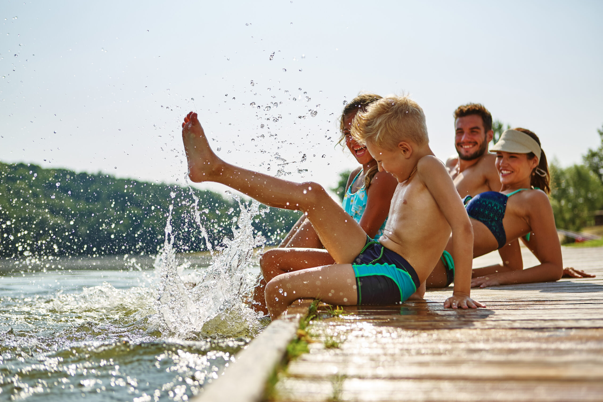 Family,Bathing,And,Splashing,Water,With,Their,Foot,At,A Photo d’une famille heureuse assise sur un quai en bois, les pieds dans l’eau